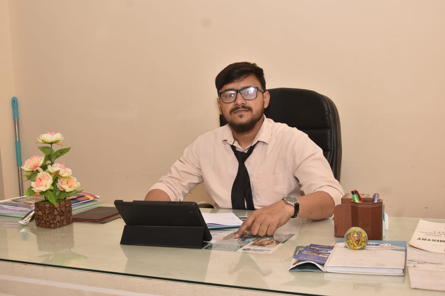 Man in pink shirt and tie sitting at a desk pointing at a brochure.